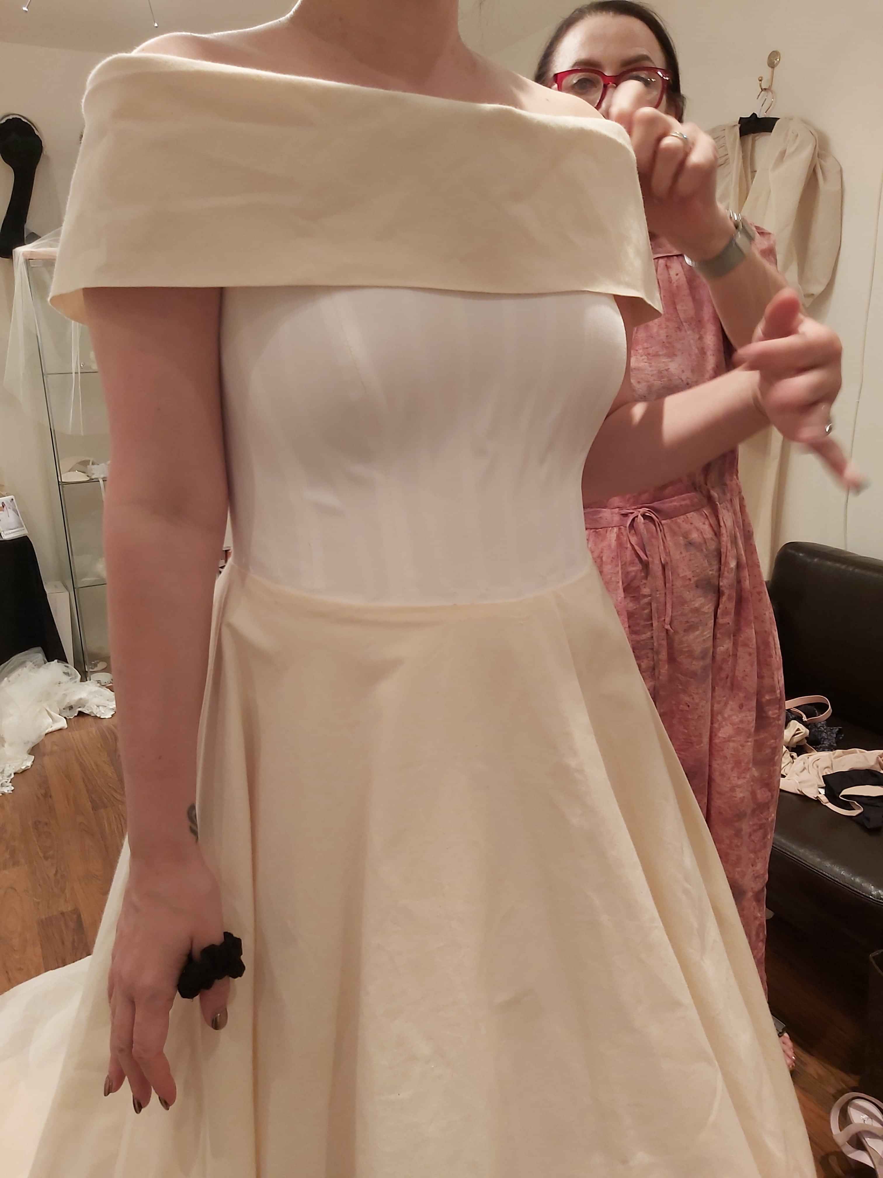 Bride at bespoke wedding dress fitting in Kate Edmondson's London atelier wearing an off -the -shoulder calico toile