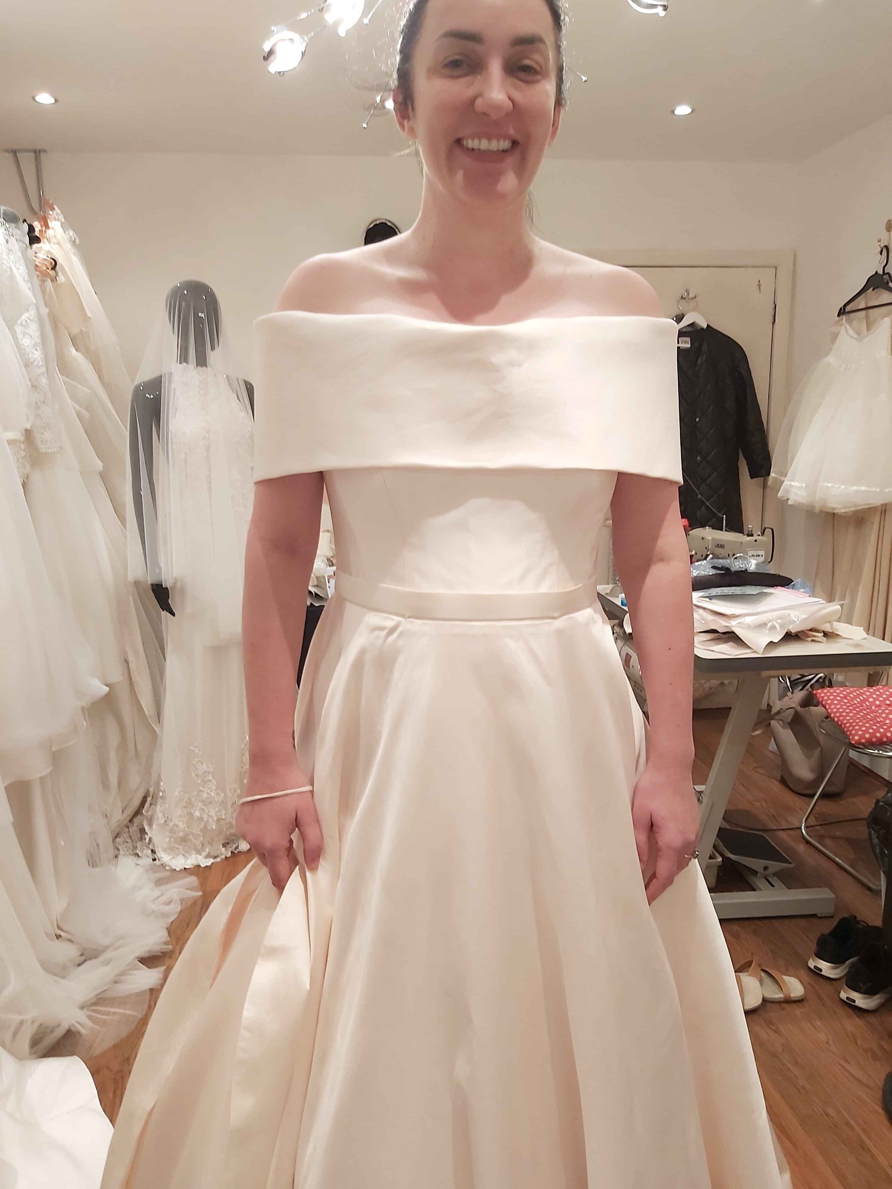 Bride in finished off-the-shoulder bespoke wedding dress by Kate Edmondson during her final fitting in the bridal studio
