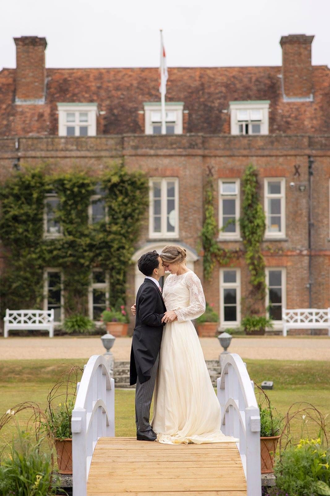 Bride and groom sharing a kiss on a white bridge at Hole Park Gardens Kent, Bride wearing bespoke wedding dress design by Kate Edmondson
