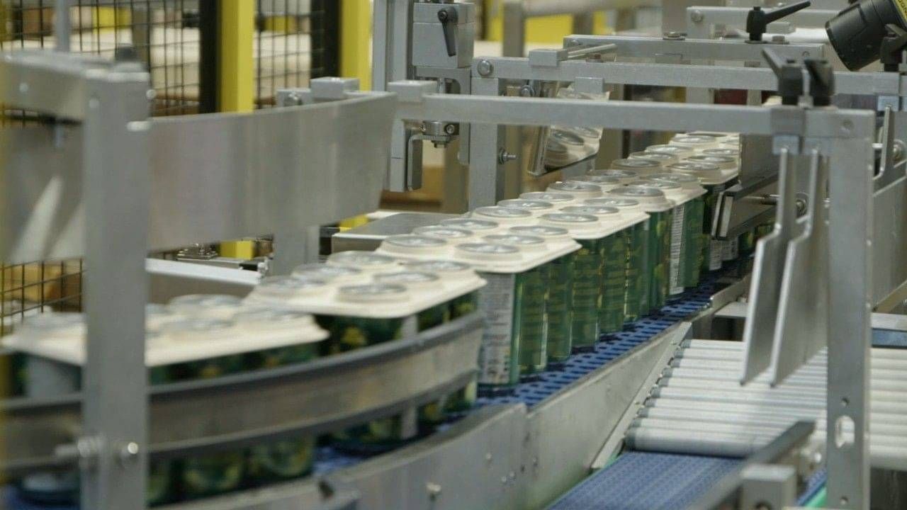 Compostable six-pack rings being applied to cans on a production line.
