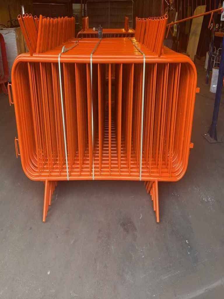 Orange powder-coated crowd control barriers stacked inside Tempfence UK factory, ready for bulk nationwide delivery